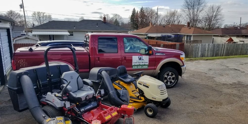 A red Williams Lawn Care Services work truck alongside two commercial lawn mowers.